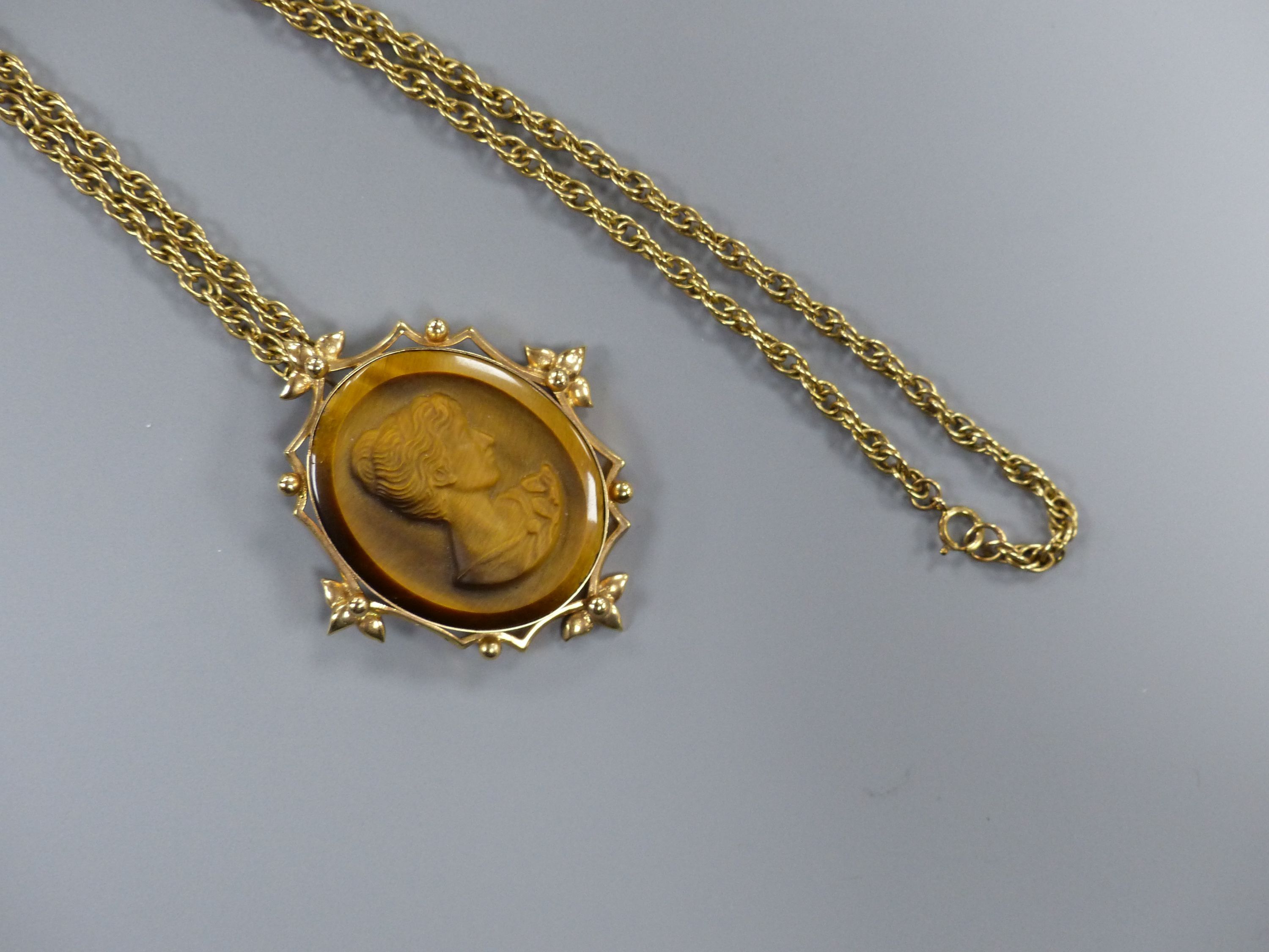 A yellow metal mounted tiger's eye quartz oval pendant, on a 9ct chain